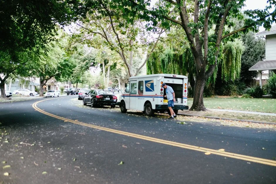 Illustrative photo of a mail carrier retrieving packages from a postal delivery van
