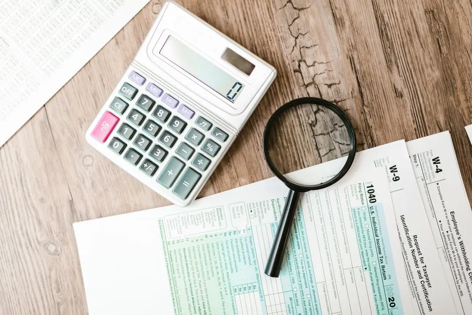 Illustrative photo of tax forms with a calculator and magnifying glass
